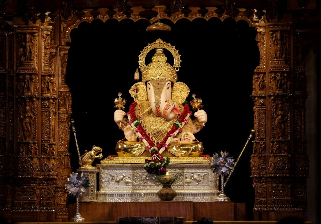 Golden Ganesha idol adorned with garlands in a wooden shrine