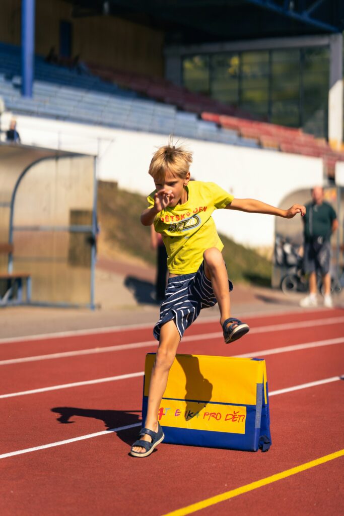 A young boy jumping over a hurdle on the track